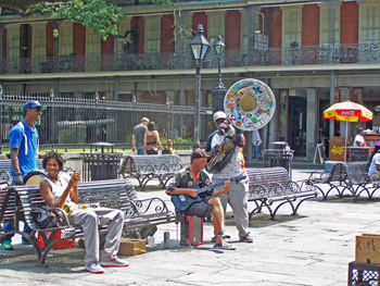 Musicians gather in Jackson Square in New Orleans, one man playing a tuba with brightly colored stickers all over the bell.