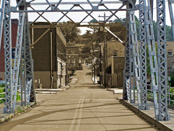 A surreal look at small town America; a color photograph of a bridge leads to the sepia tone of small town America buildings.